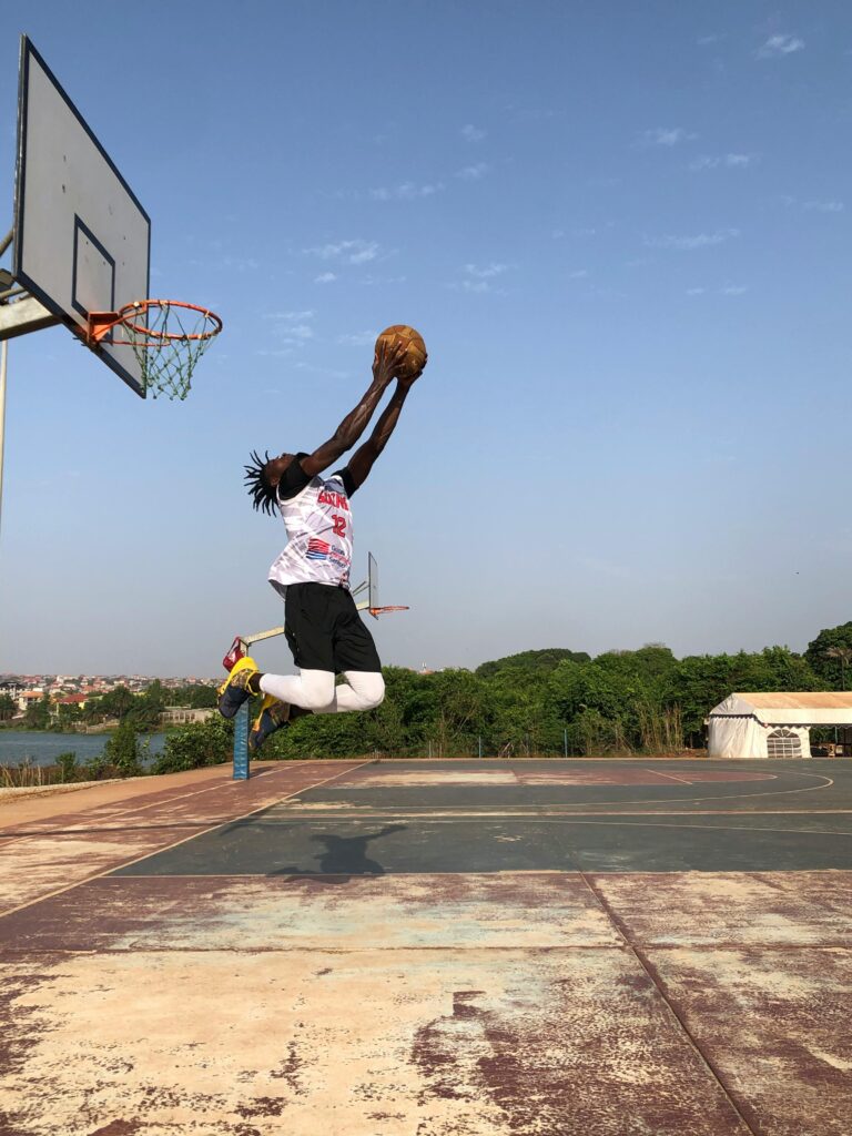 Athlete performing a powerful dunk on an outdoor basketball court under a clear blue sky.